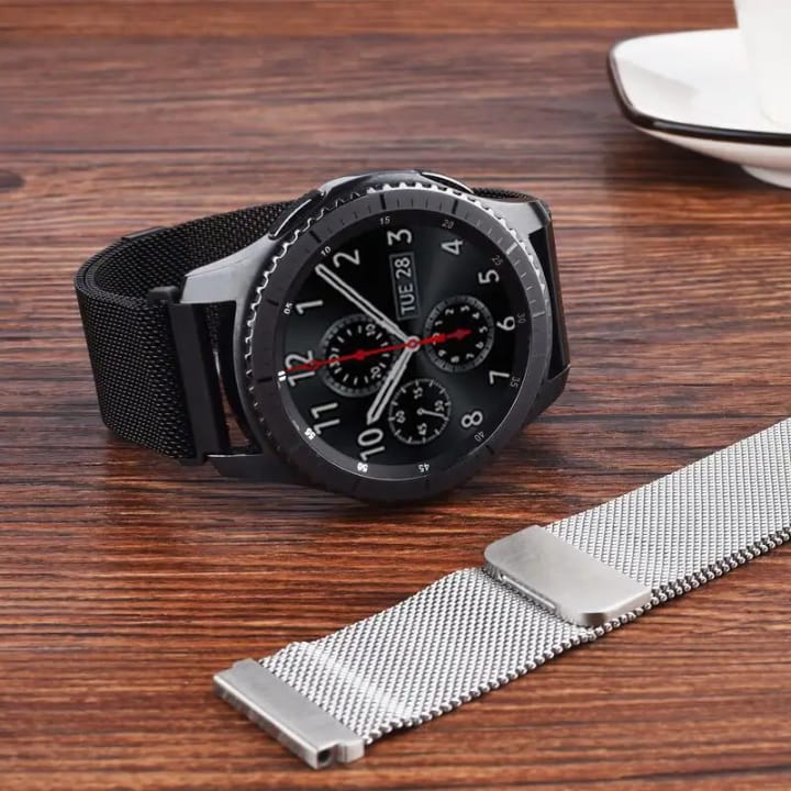 The Loop in black on a round smartwatch, with a silver band lying beside it